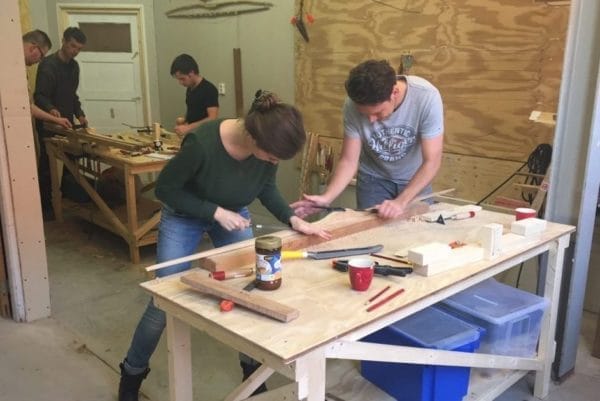 Deelnemers van de workshop zelf een houten handboog maken werken in de werkplaats aan hun bogen.