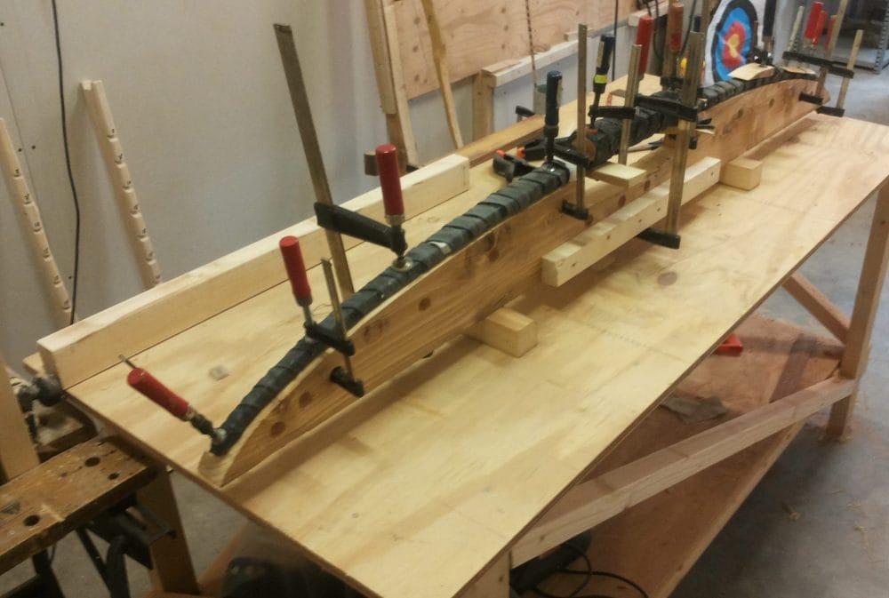 Tijdens een workshop zelf een handboog maken, liggen de onderdelen van een houten boog op de werkbank, klaar om in de mal verlijmd te worden.