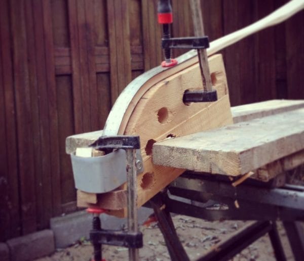 Robinia hout van een werparm van een boog is gestoomd en wordt nu met een mal en klemmen gebogen tot recurve.