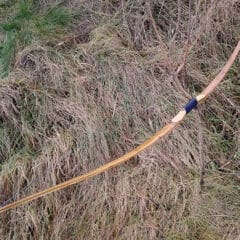 Handgemaakte houten boog van essenhout op een achtergrond van gras, met smalle uiteinden voor snelheid.