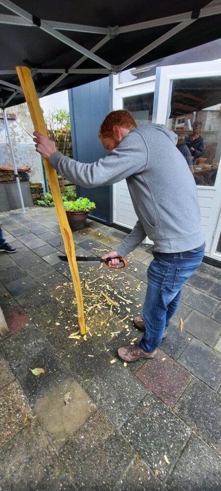 Bij de workshop zelf een boog maken, gebruikt een deelnemer een mes om de houten boogstaaf van osage bij te schaven.